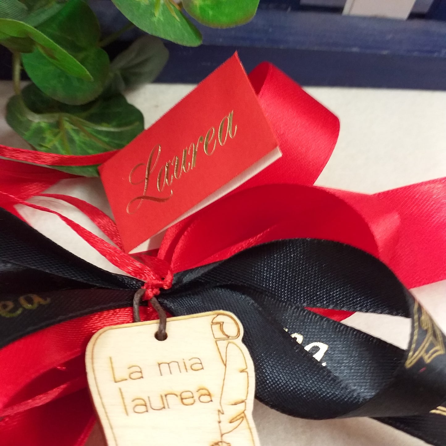 primo piano bigliettino e simbolo fiocco coccarda segnaposto fai da te o confezionato packaging rosso-nero ciondolo green legno pirografato la mia laurea calamaio pergamena