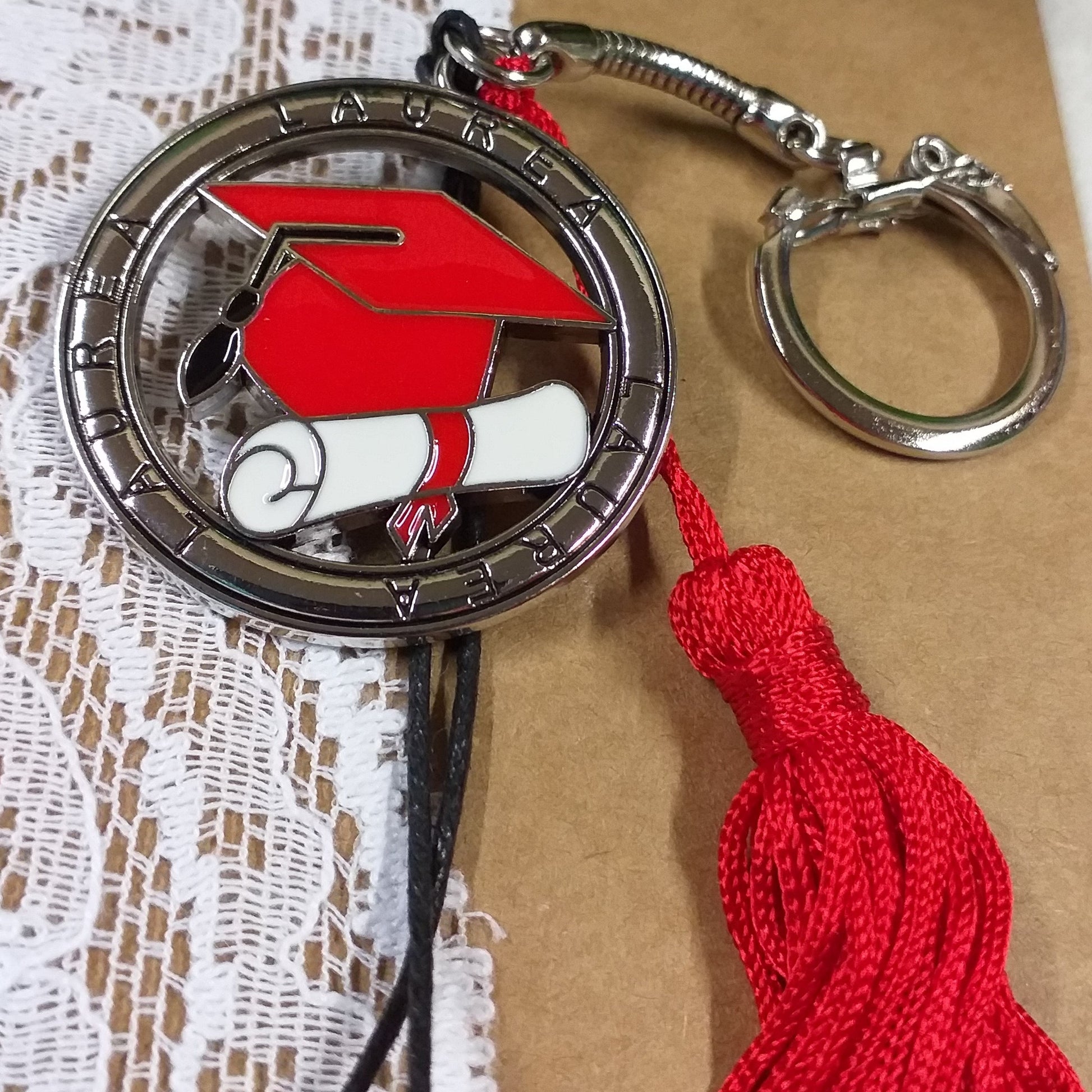 primo piano portachiavi tocco cappello laurea rosso ciondolo smaltato pergamena bianca nappina rossa scritta laurea sul tondo metallo zama della bomboniera gancio catenina