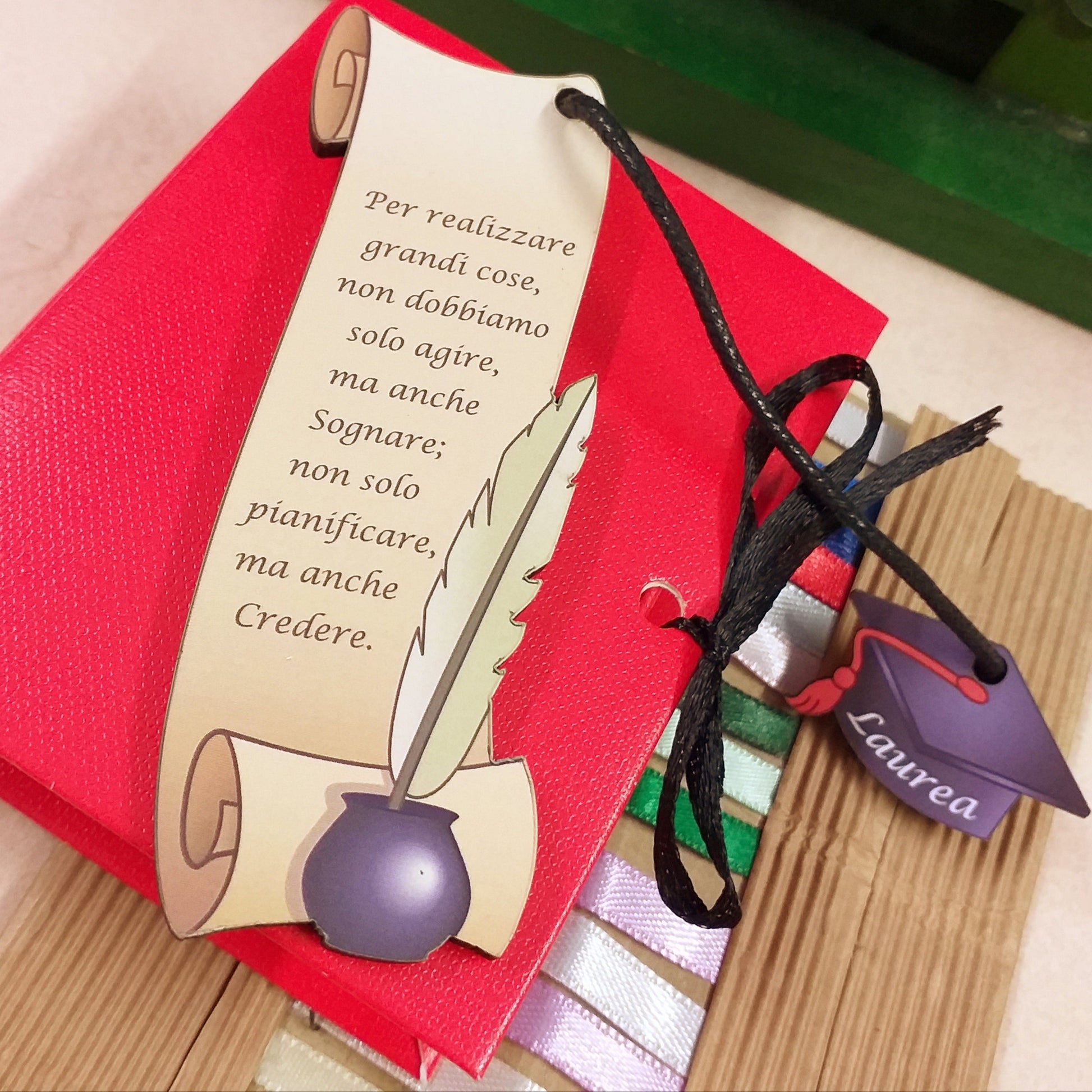 Per realizzare grandi cose non dobbiamo solo agire ma anche sognare  non solo pianificare ma anche credere frase scritta stampata sul segnalibro legno pergamena inchiostro calamaio ciondolo tocco laurea cappello nero cordino confezionato bomboniera libro cartoncino rosso portaconfetti nastrino